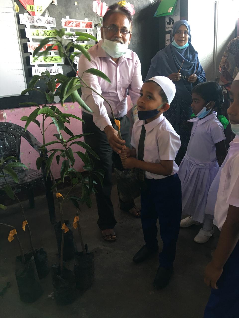 Young participant holding a tree prepared for planting during a Pottuvil environmental activity.